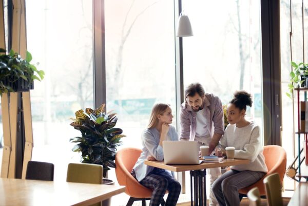 Three people collaborating at a table with a laptop and coffee in a modern office space.