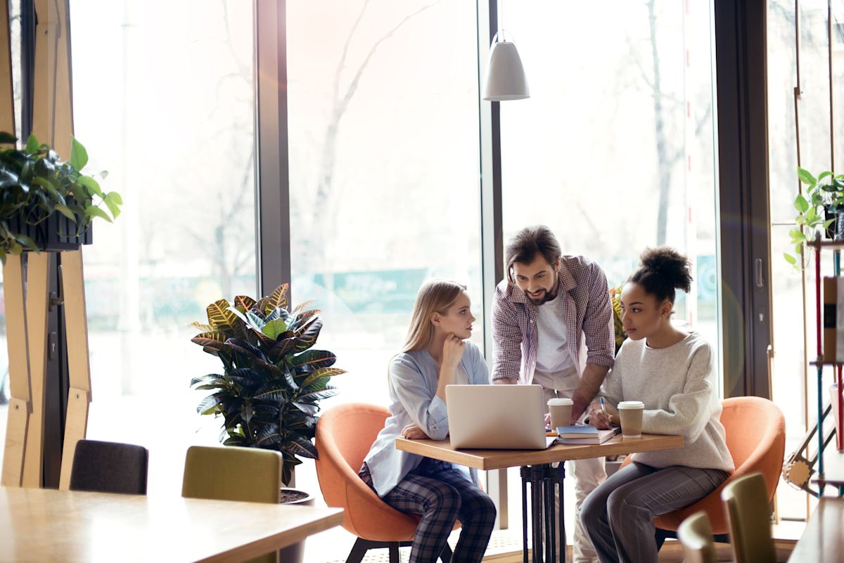 Three people collaborating at a table with a laptop and coffee in a modern office space.