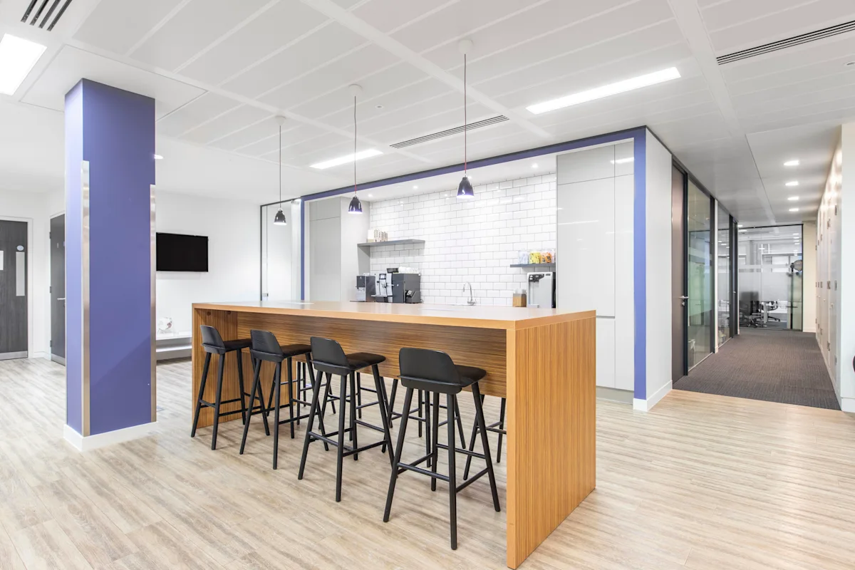 A modern office kitchen at 63 St Mary Axe, London, featuring a wooden counter with black stools.