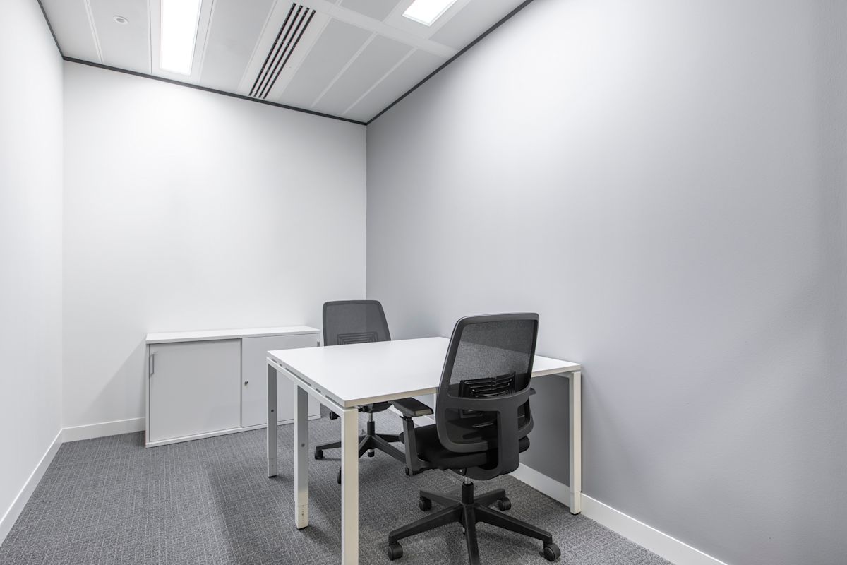 A small, minimalist office space with two black chairs, a white desk, and a storage cabinet.