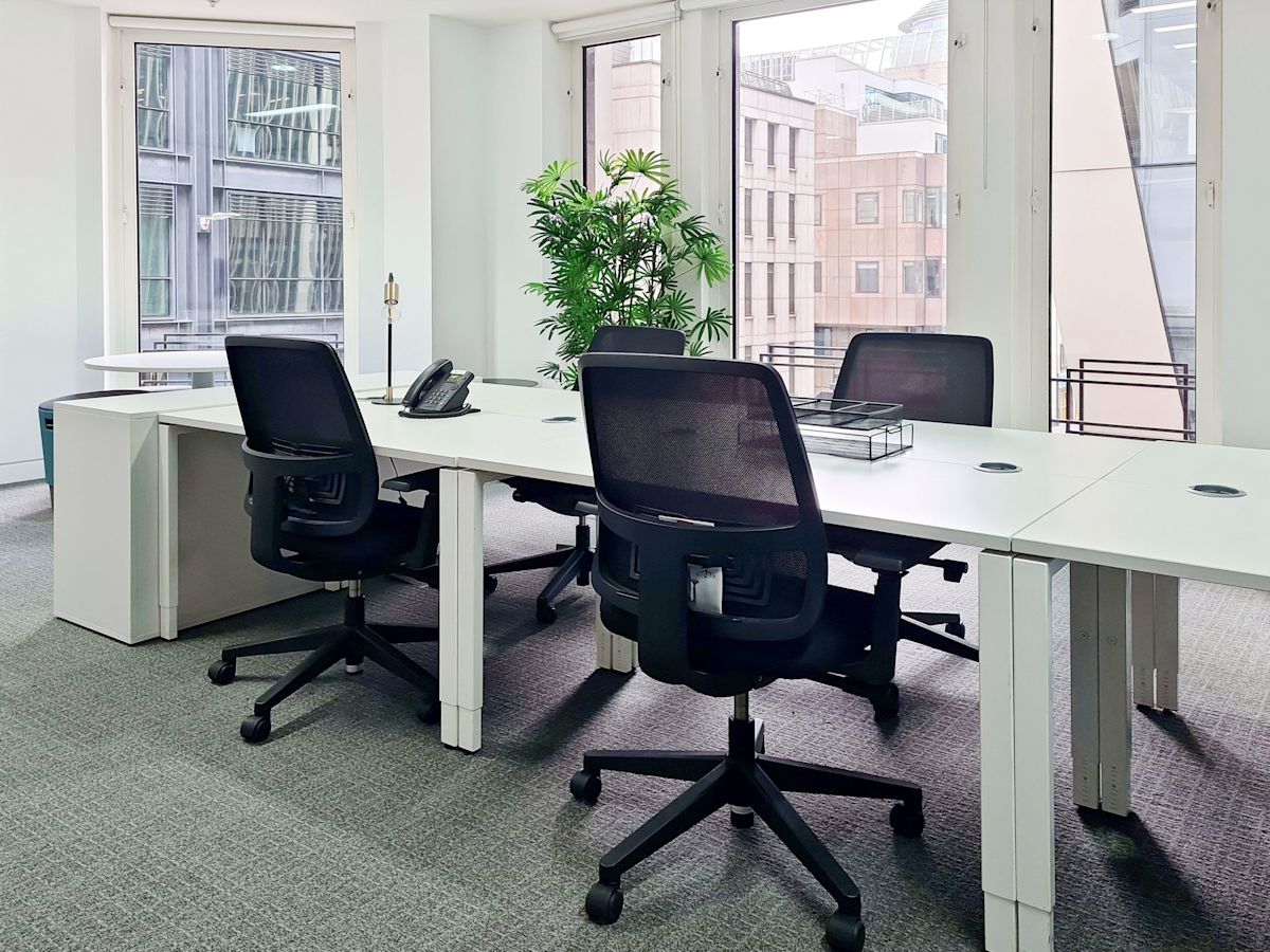 Modern office space with several desks and chairs overlooking a city view through large windows.