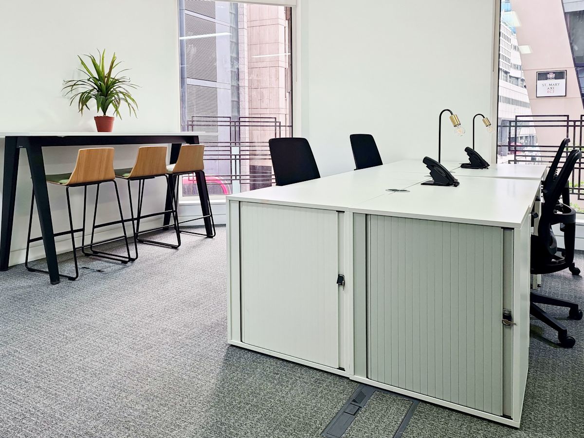 A modern office space at St Mary Axe 63, London, featuring a meeting area with a table, chairs, and a potted plant.