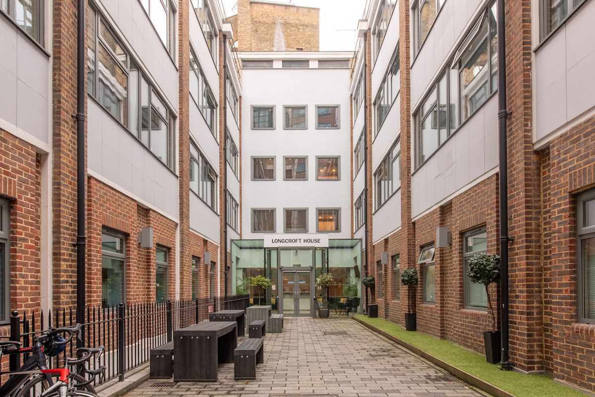 The image shows an exterior view of Longcroft House on Victoria Avenue, London, with a courtyard featuring benches and bicycles.