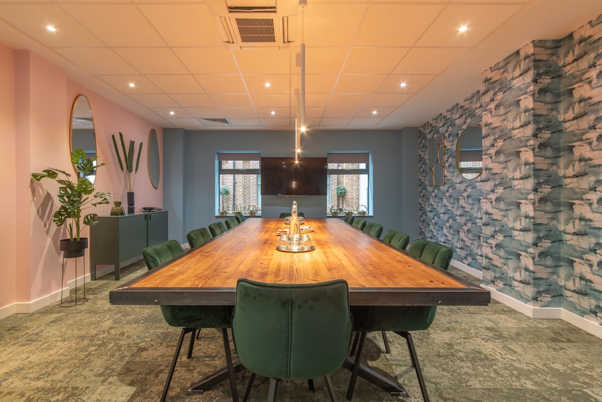 A modern conference room with a long wooden table, green chairs, and decorative wall mirrors.