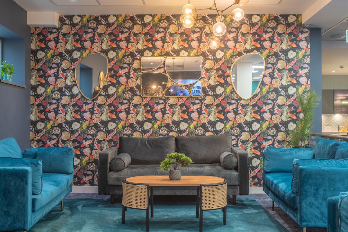 A stylish living room with colorful patterned wallpaper, blue and gray sofas, and a wooden coffee table.