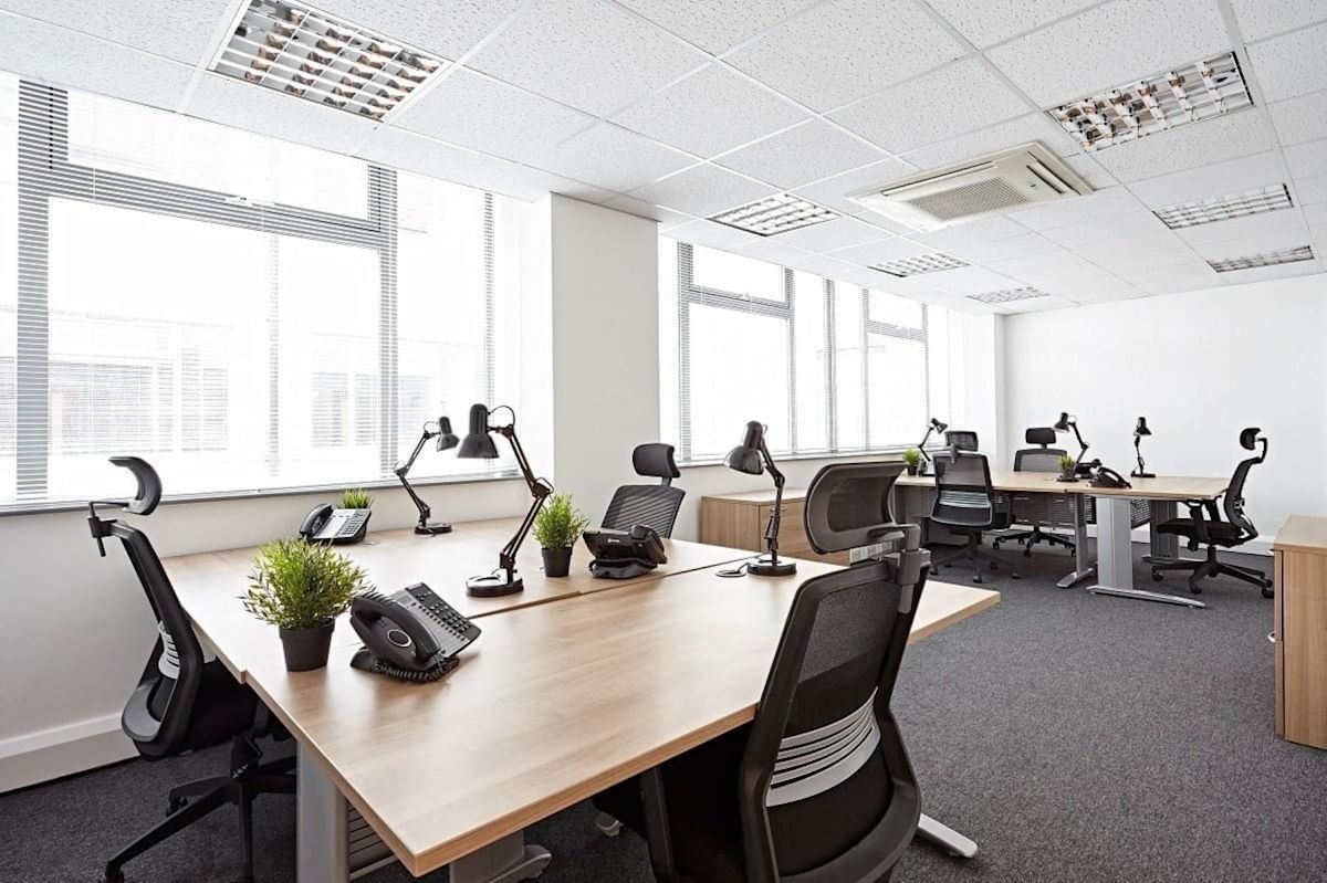 A modern, well-lit office space with multiple desks, chairs, and plants.