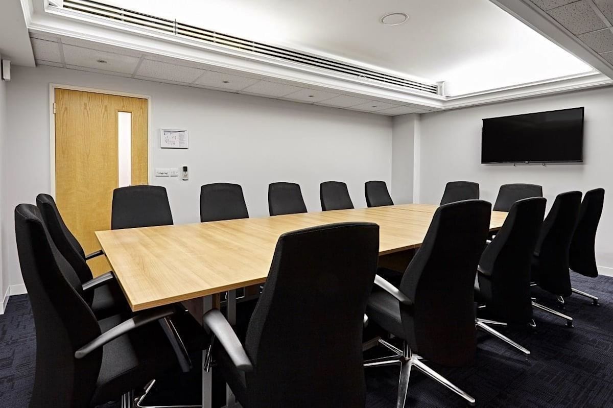 A modern conference room with a long wooden table and black chairs.