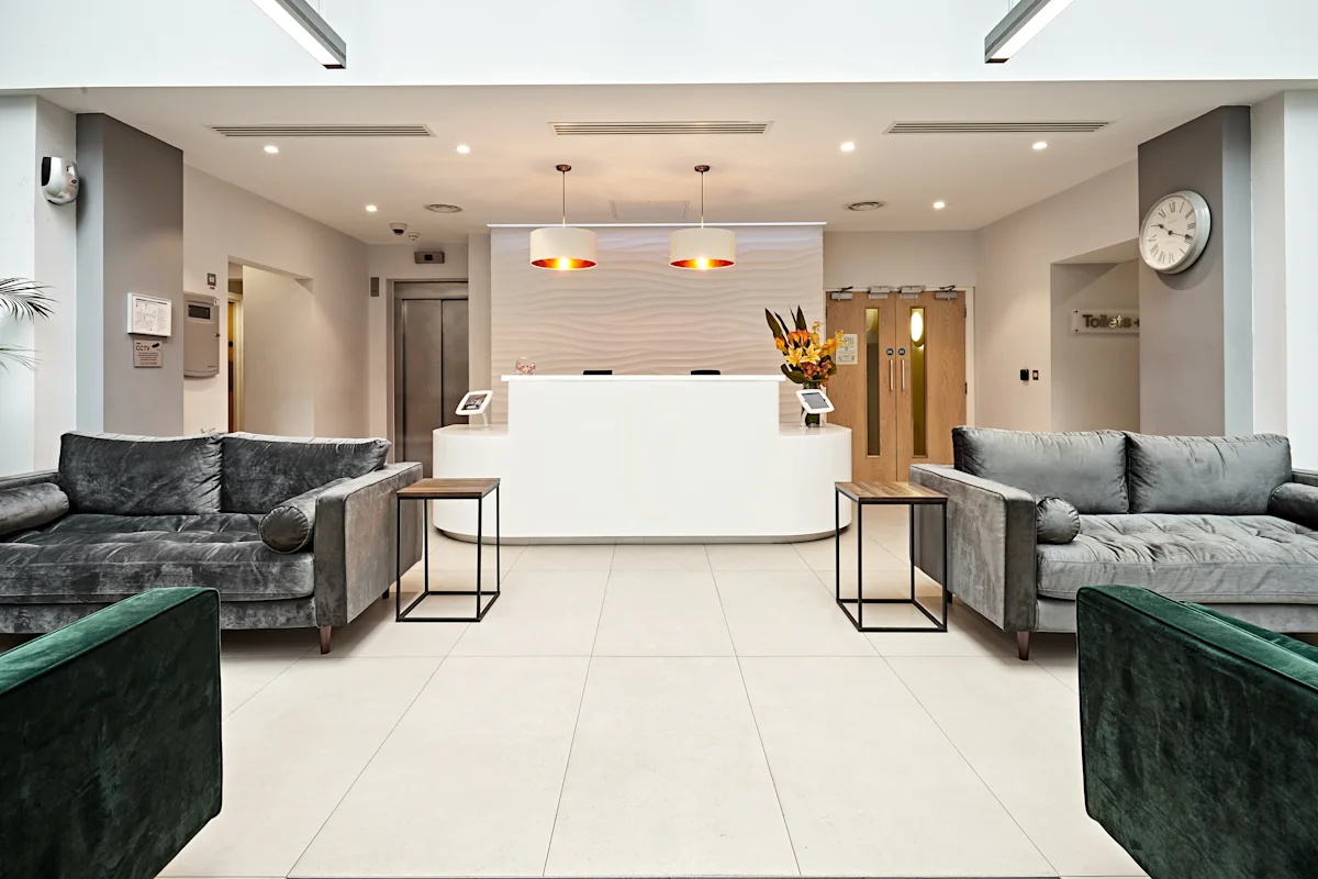 Modern reception area with two grey sofas, a white desk, and warm lighting.