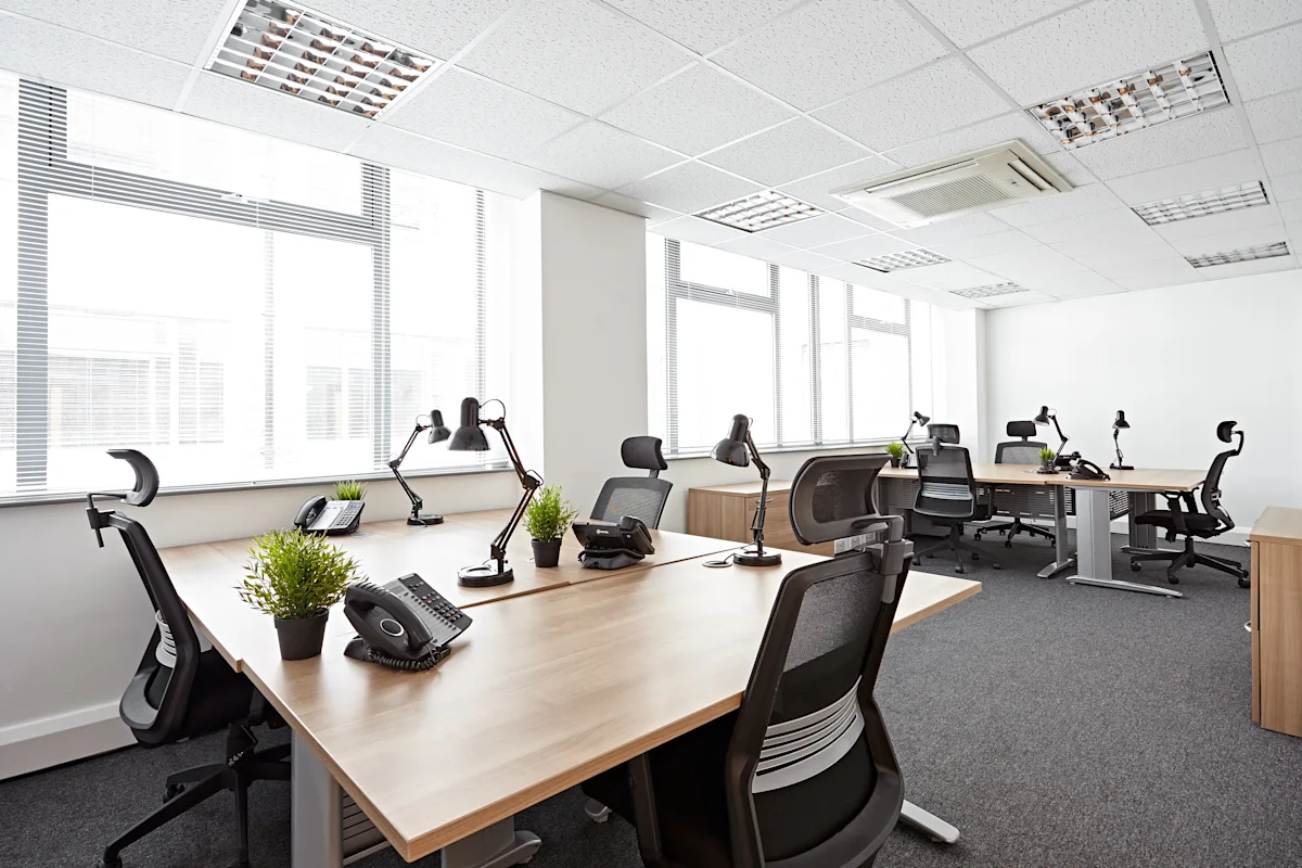A modern office space with desks, chairs, desk lamps, phones, and small plants, located on Victoria Avenue, London.