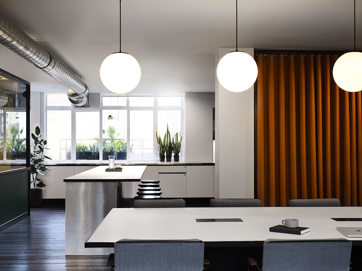 Modern office space with large windows, orange curtain, and minimalist furnishings at Wardour Street 151 in London.