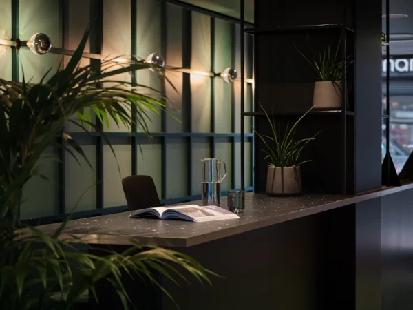 A modern office reception area with plants, a desk, an open book, and dim lighting.