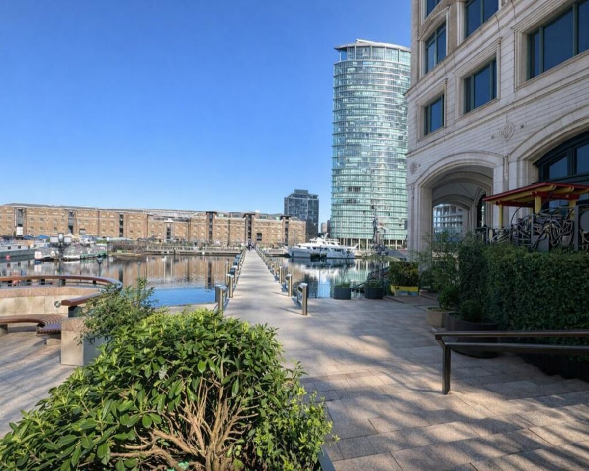 A scenic view of Westferry Circus in London, showcasing a waterfront walkway and modern buildings under a clear blue sky.