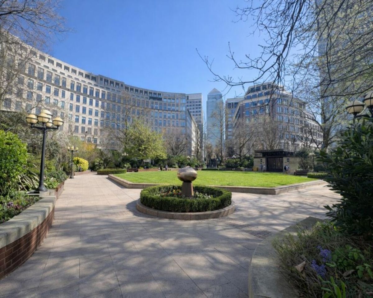 A sunny view of Westferry Circus in London, featuring a landscaped garden surrounded by modern buildings.
