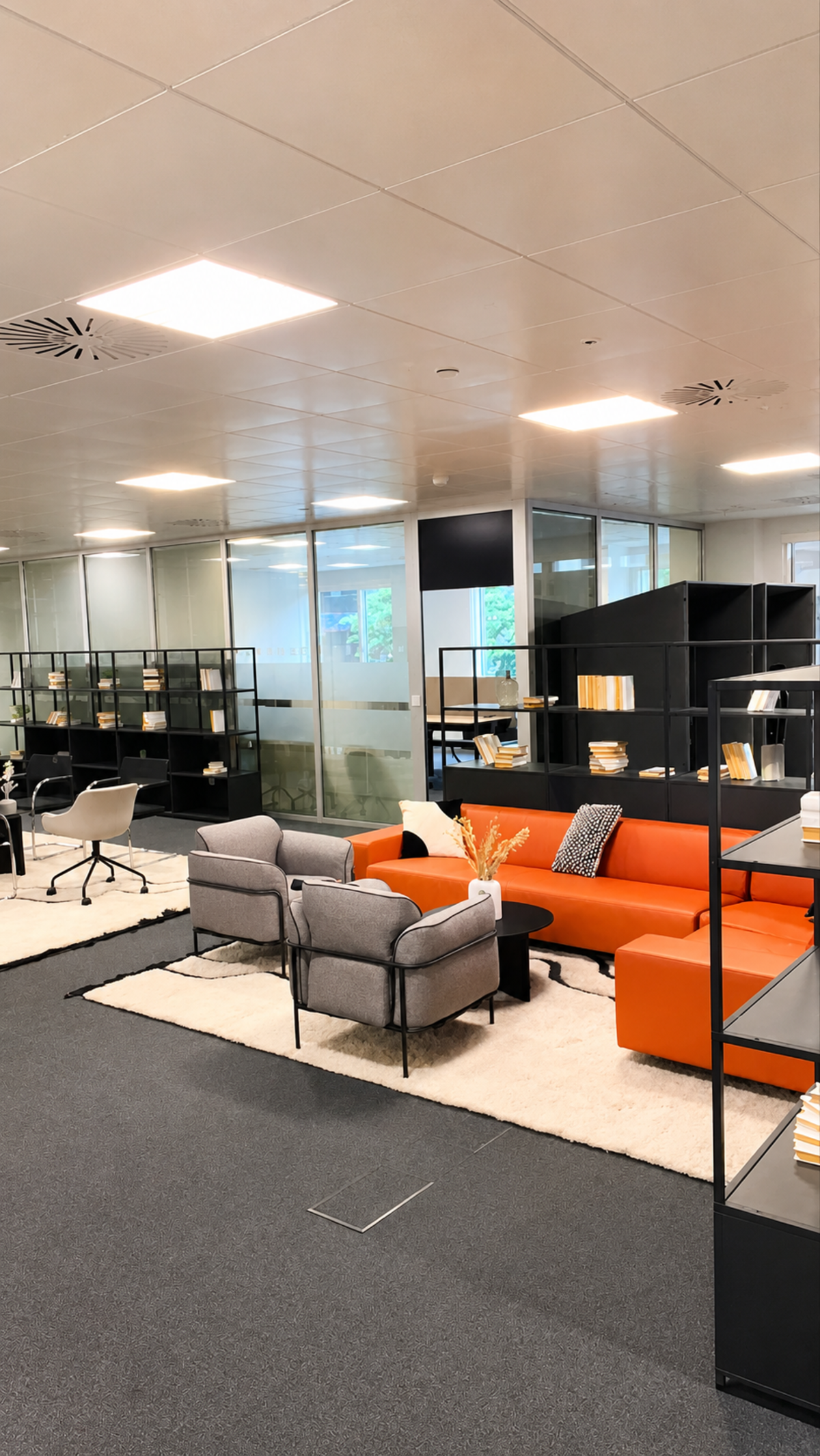 A modern office space with orange and gray seating, bookshelves, and glass partition walls.