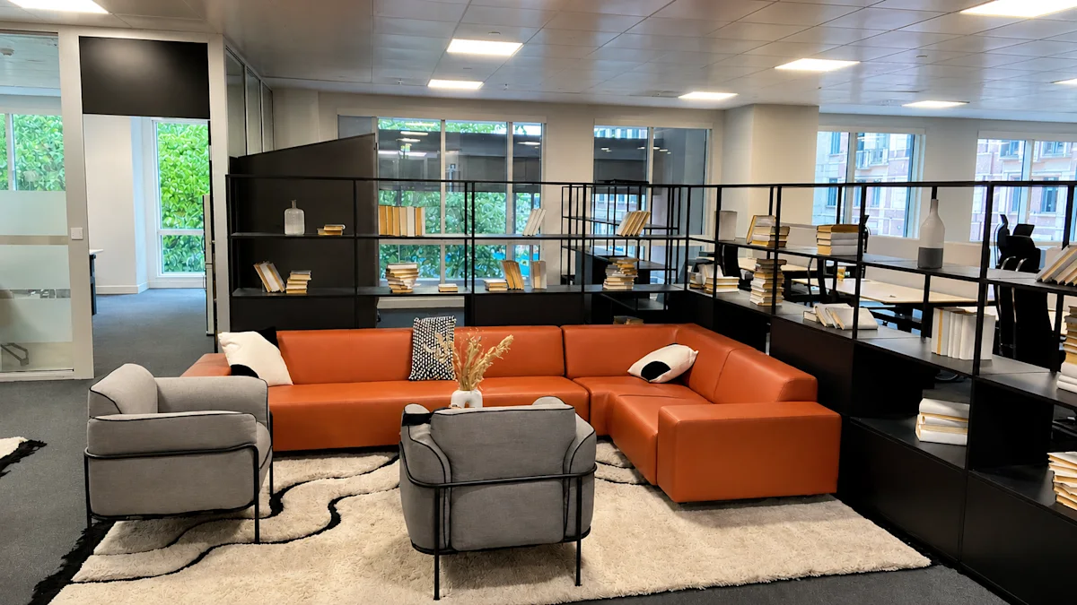 A modern office lounge area with a brown sofa, grey armchairs, and bookshelves at Westferry Circus, London.