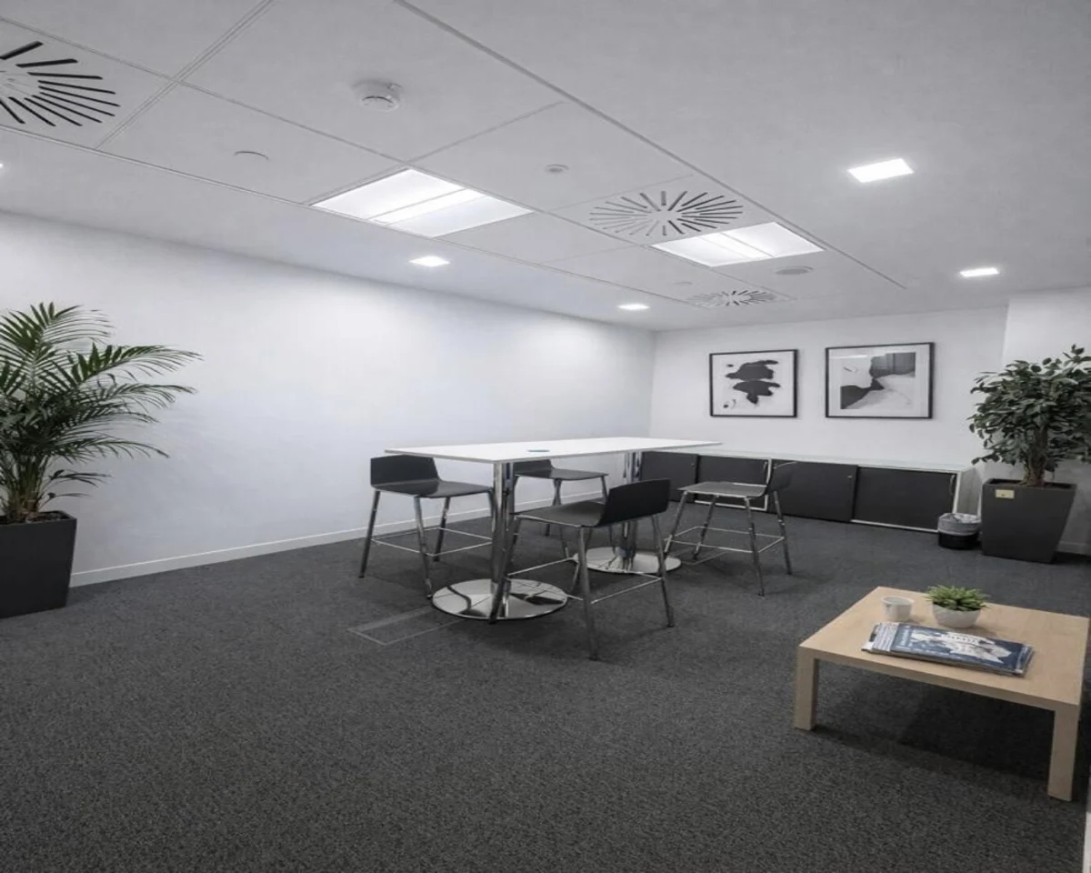 A modern office lounge area with a table, chairs, potted plants, and abstract wall art.